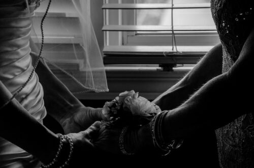 grayscale photography of two woman holding hands near window blinds