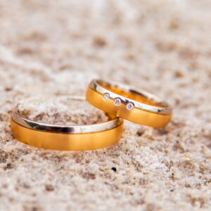 two gold wedding rings laying on the sand