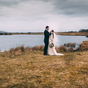 bride and groom photography on brown grass near body of water during daytime